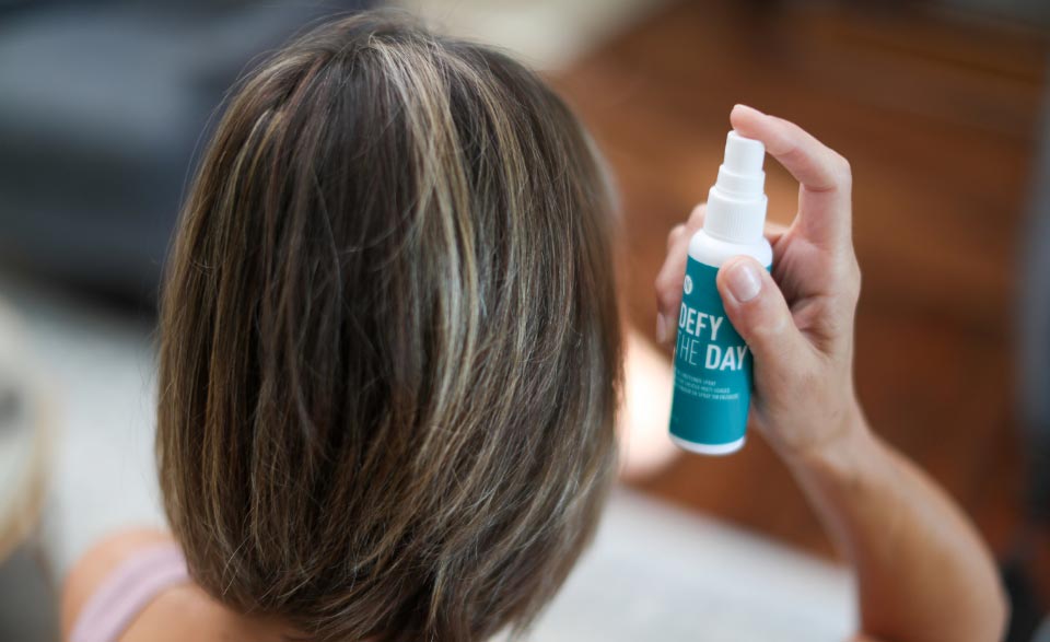 A woman spraying the Defy the Day Leave-in Conditioner Spray in her hair.